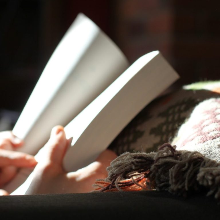 Personas leyendo un libro en un entorno acogedor y con una manta encima.
